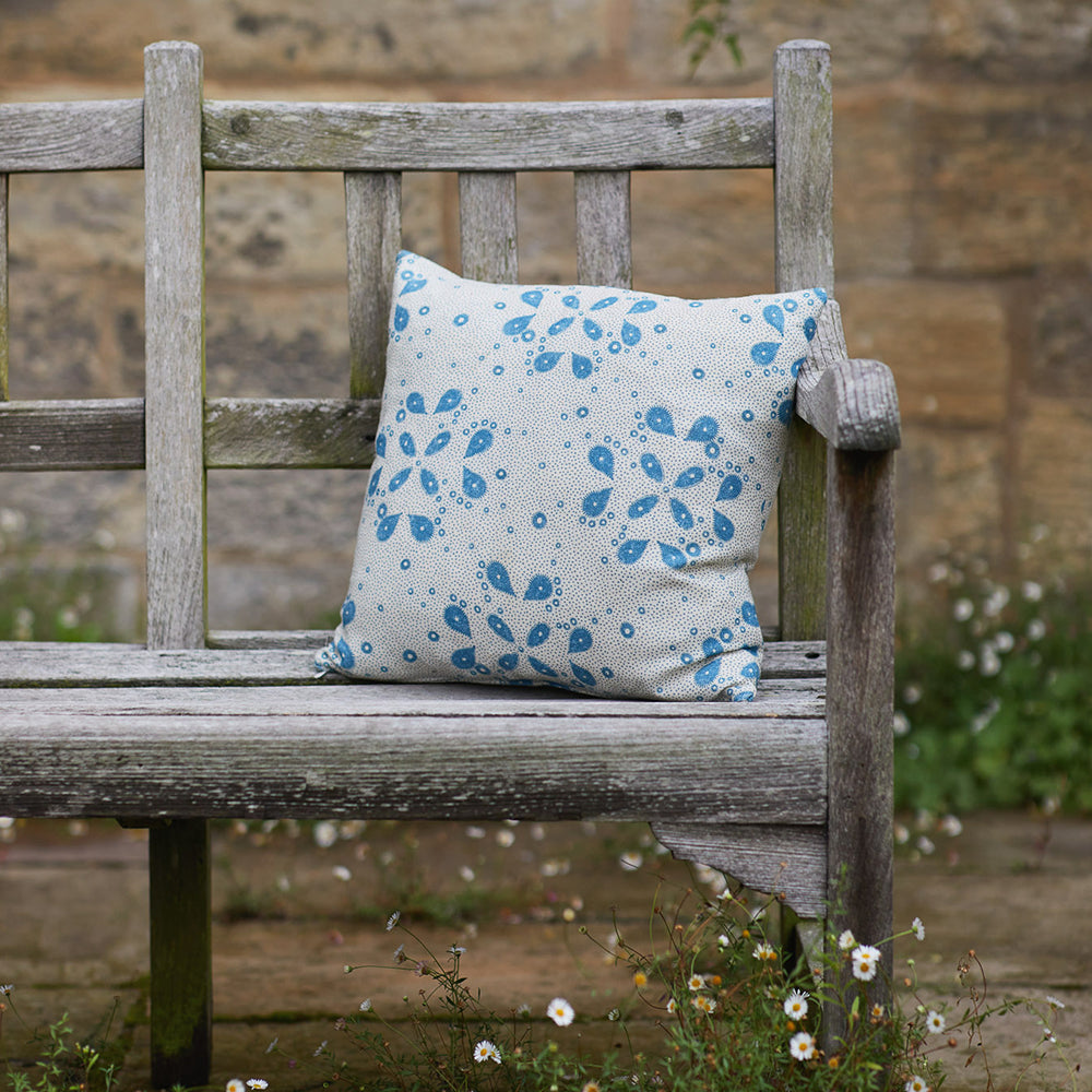 A wooden bench topped with a throw pillow in a playful paisley print in blue on a tan field.