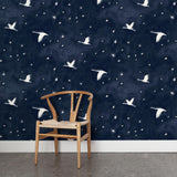 A wooden chair stands in front of a wall papered in a print of birds and stars in white on a navy watercolor field.