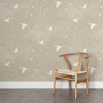 A wooden chair stands in front of a wall papered in a print of birds and stars in white on a tan watercolor field.