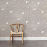 A wooden chair stands in front of a wall papered in a print of birds and stars in white on a light gray watercolor field.