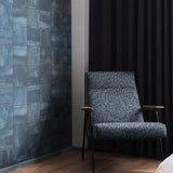 A patterned armchair stands in front of a wall papered in square leather tiles in mottled navy.