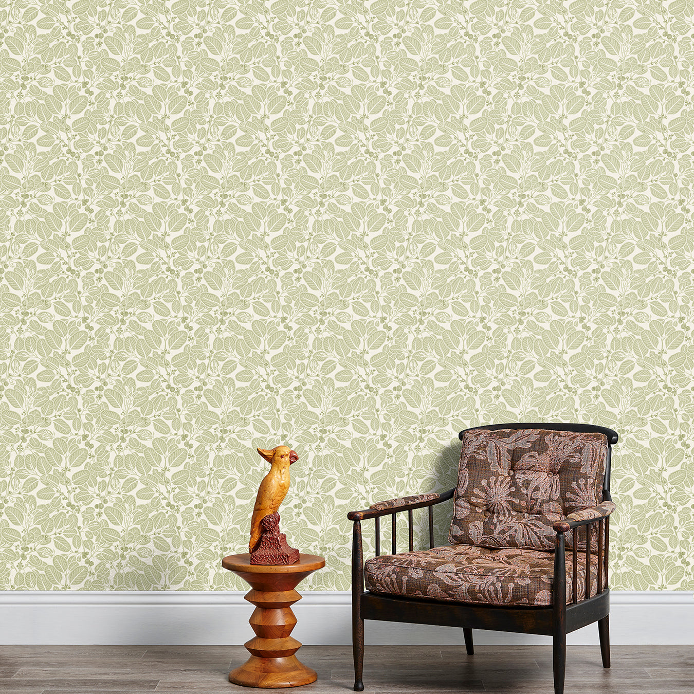 Armchair and end table in front of a wall papered in a dense leaf and stem print in sage and white.