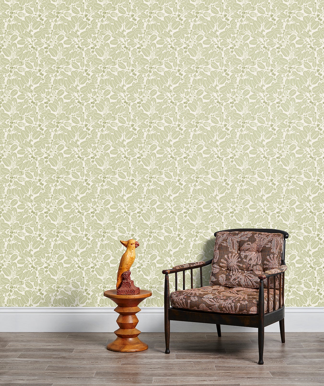 Armchair and end table in front of a wall papered in a dense leaf and stem print in sage and white.