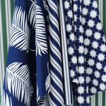 Hanging swatches of performance fabric in blue and white in a palm frond, stripe and moroccan star pattern on a green and white striped background.