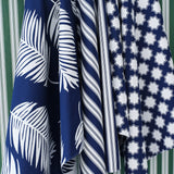 Hanging swatches of performance fabric in blue and white in a palm frond, stripe and moroccan star pattern on a green and white striped background.