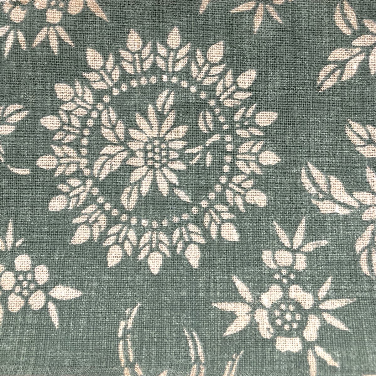 Detail of fabric in a geometric floral print in cream on a sage field.