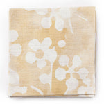 A stack of fabric swatches in a painterly branch print in white on a yellow watercolor field.