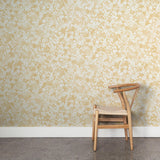 A wooden chair stands in front of a wall papered in a painterly branch print in white on a yellow watercolor field.