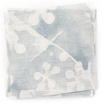 A stack of fabric swatches in a painterly branch print in white on a blue-gray watercolor field.