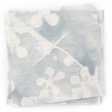 A stack of fabric swatches in a painterly branch print in white on a blue-gray watercolor field.