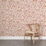 A wooden chair stands in front of a wall papered in a painterly branch print in white on a coral watercolor field.