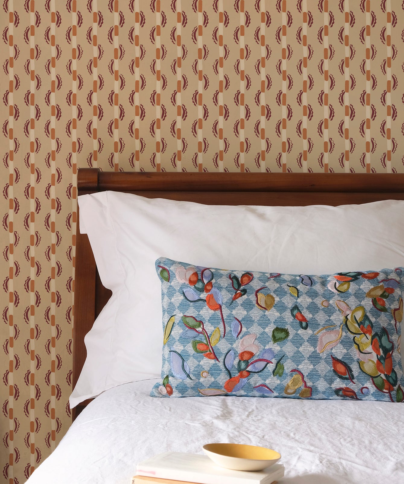Bed with patterned headboard, floral pillow, and books on a brown striped wallpaper.