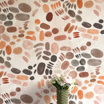 A vase of flowers stands in front of a wall covered in a playful paint blotch print in brown and orange on a cream field.