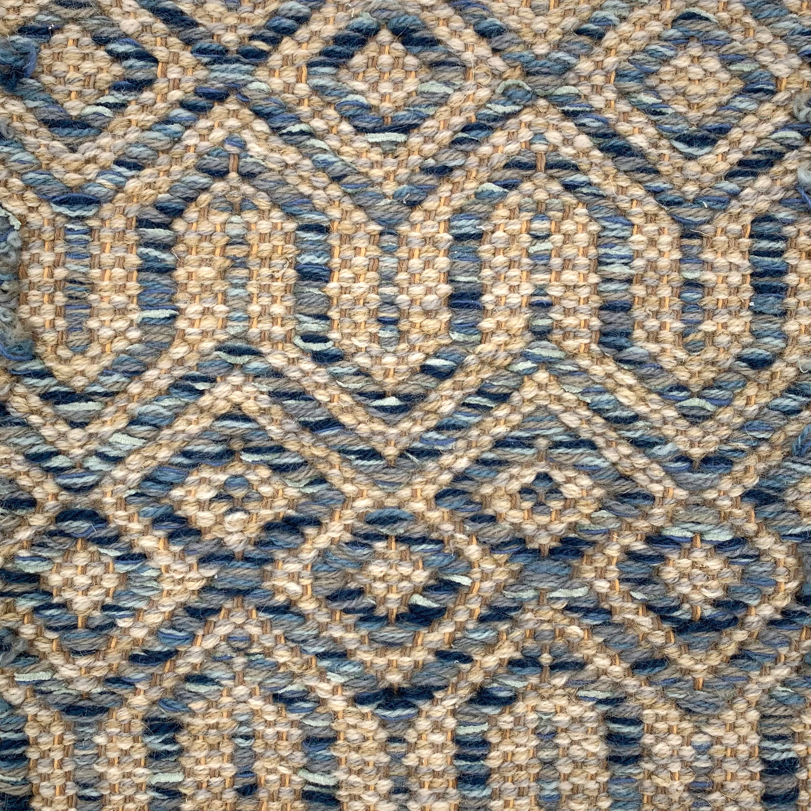 Handwoven carpet in a complex geometric lattice design in shades of blue on a beige field. 