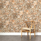 A wooden chair stands in front of a wall papered in a painterly small-scale diamond print in cream, brown and orange.