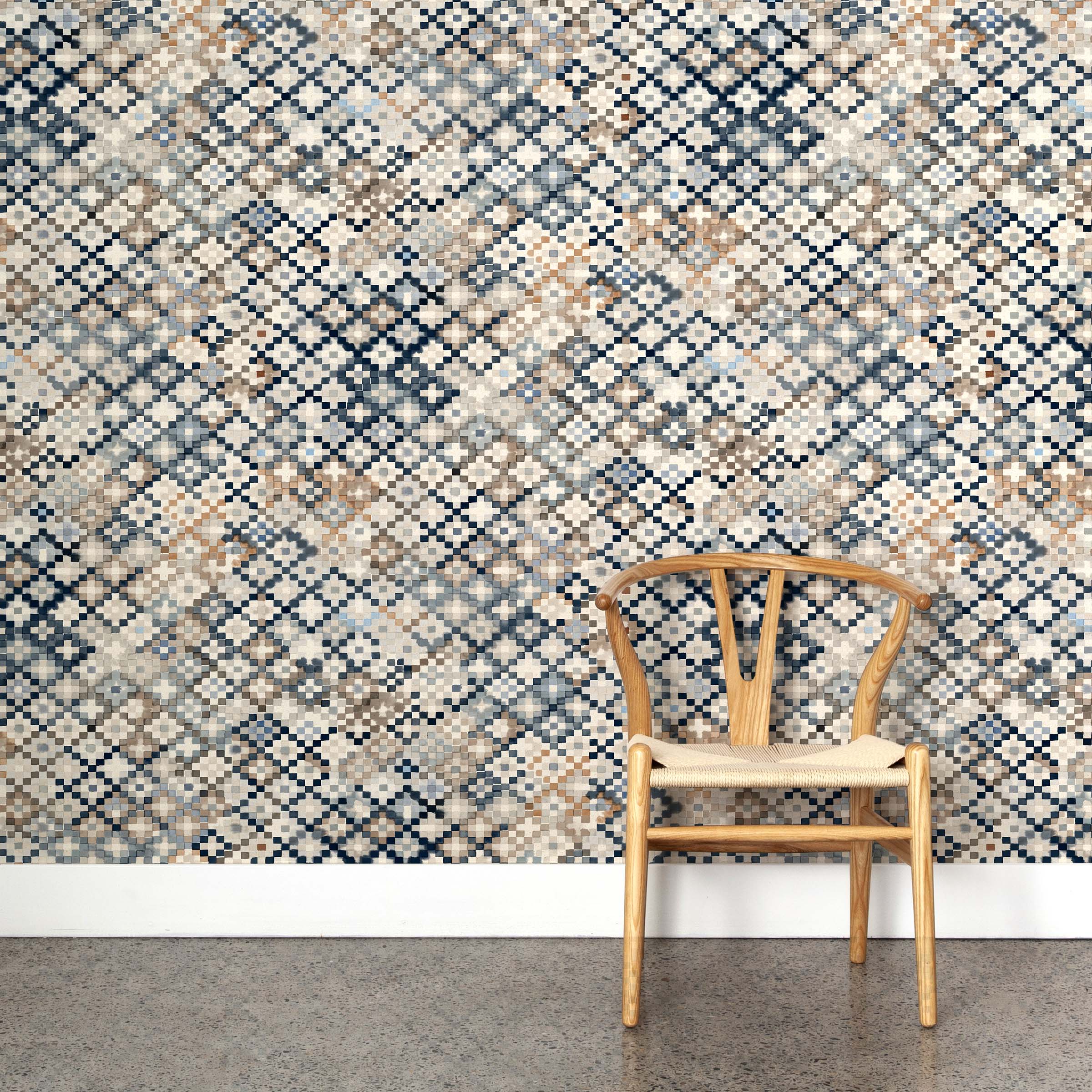 A wooden chair stands in front of a wall papered in a painterly small-scale diamond print in cream, brown, blue and gray.