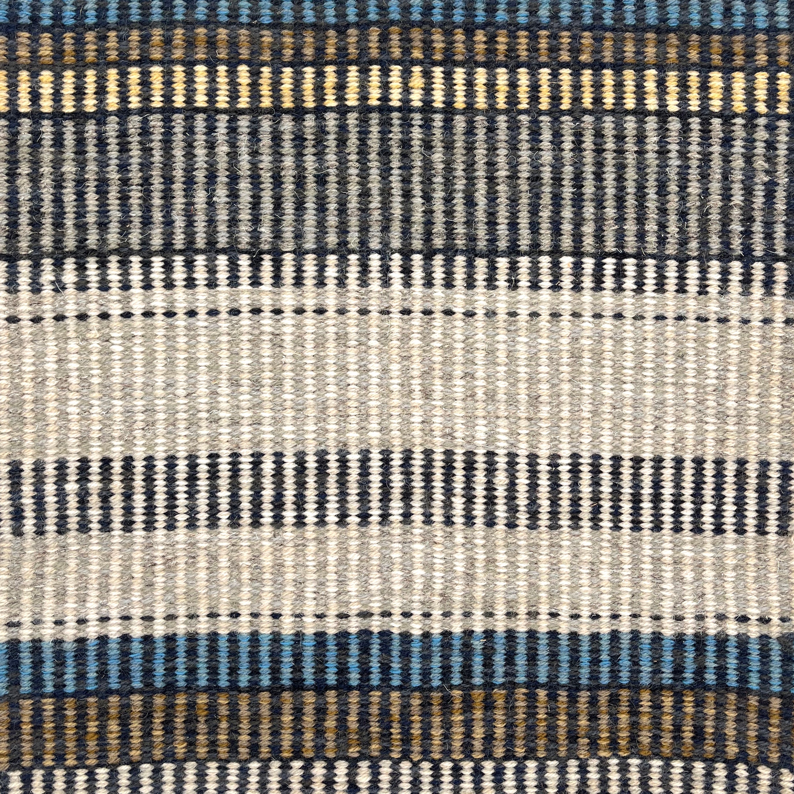 Handwoven rug detail in a stripe design in blue, yellow, tan, cream, and grey