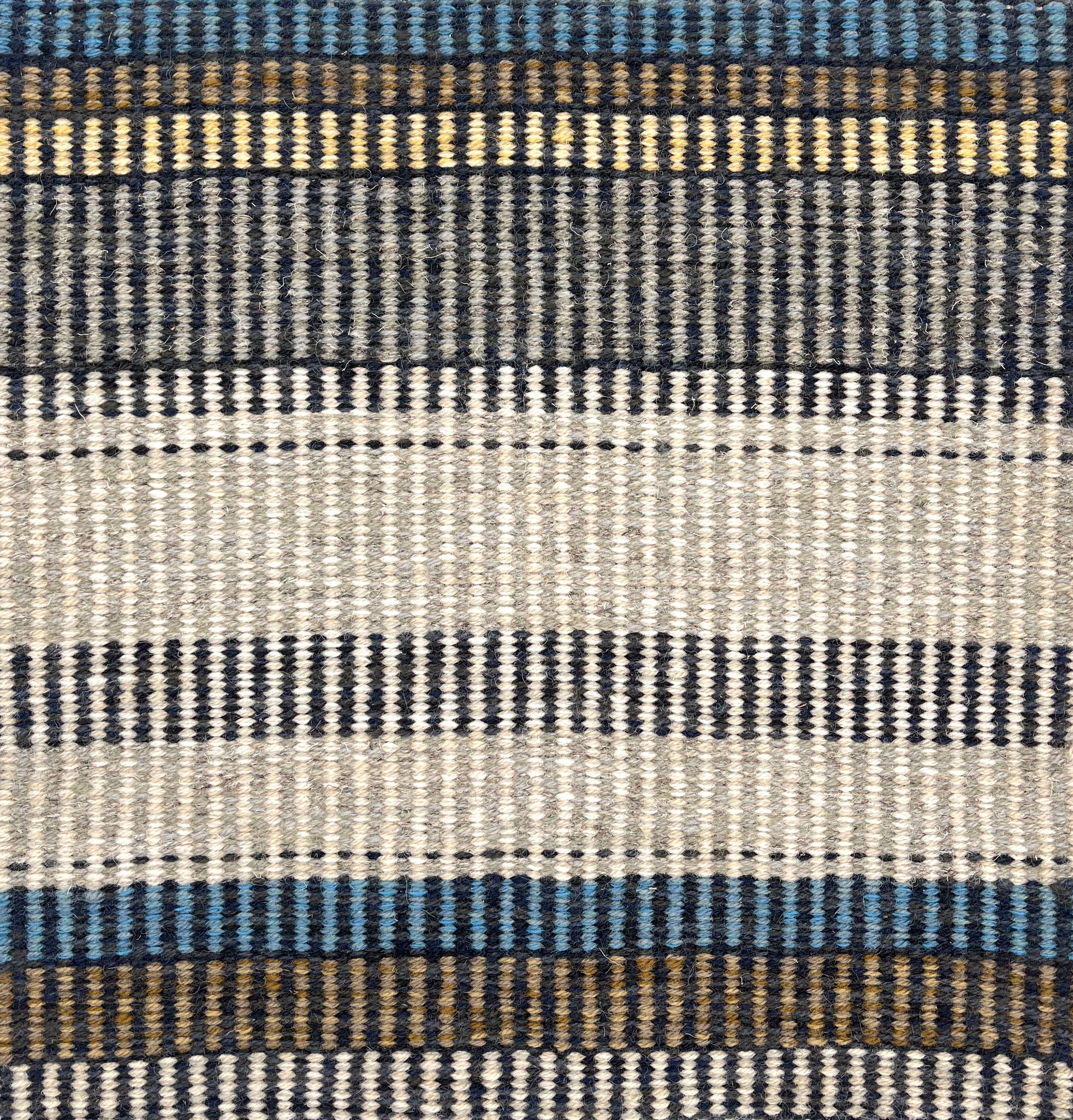 Handwoven rug detail in a stripe design in blue, yellow, tan, cream, and grey