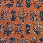 Detail of fabric in a repeating vase and plant print in navy on a mottled rust field.