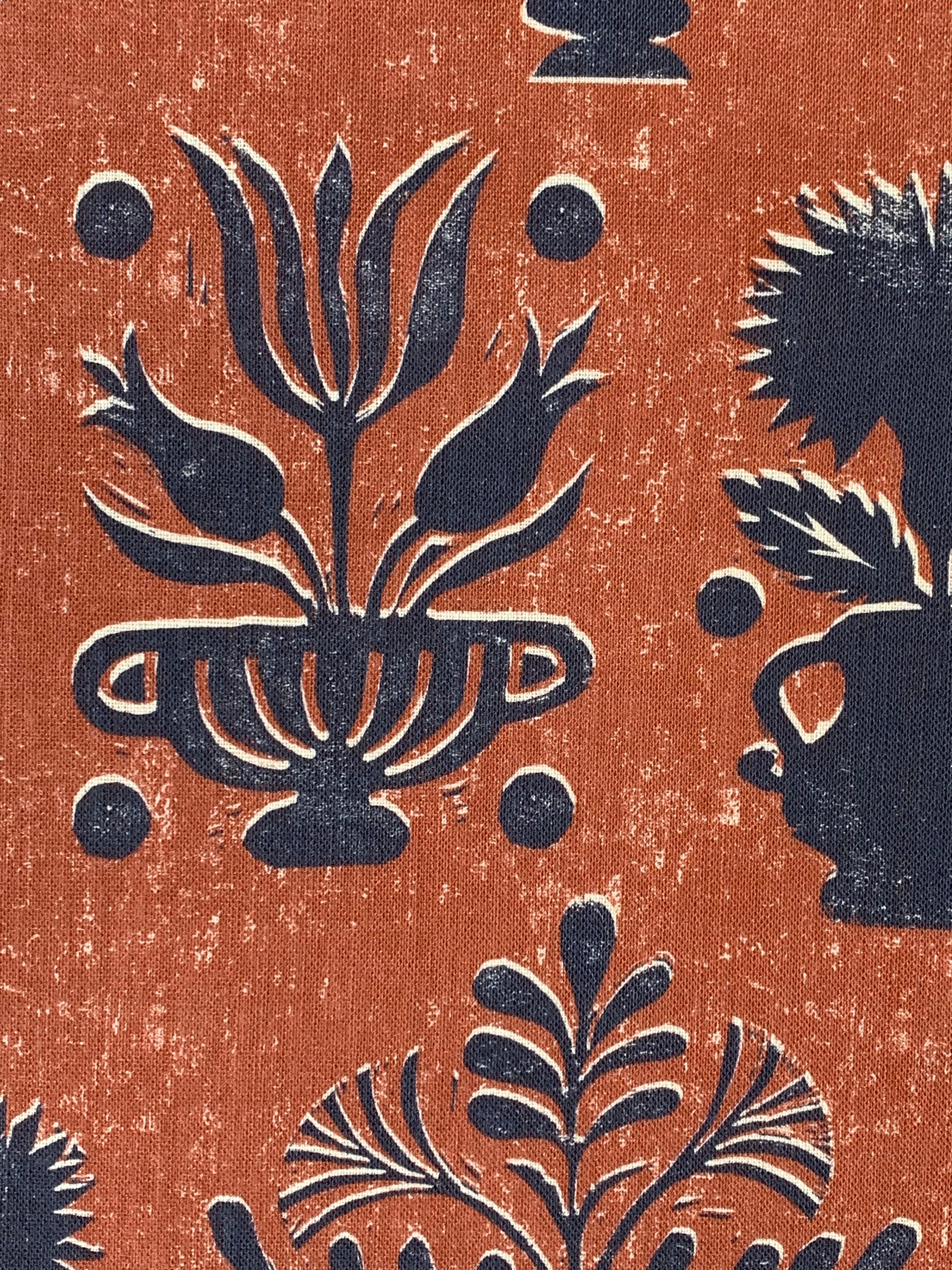 Close-up of fabric in a repeating vase and plant print in navy on a mottled rust field.