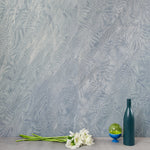 A table with knick knacks stands in front of a wall papered in an abstract ridged texture in metallic blue-gray.