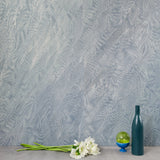 A table with knick knacks stands in front of a wall papered in an abstract ridged texture in metallic blue-gray.