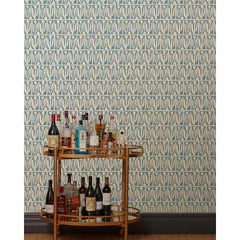 A bronze bar cart in front of a wall papered in an abstract tulip print in a repeating stripe on a dusty blue field.
