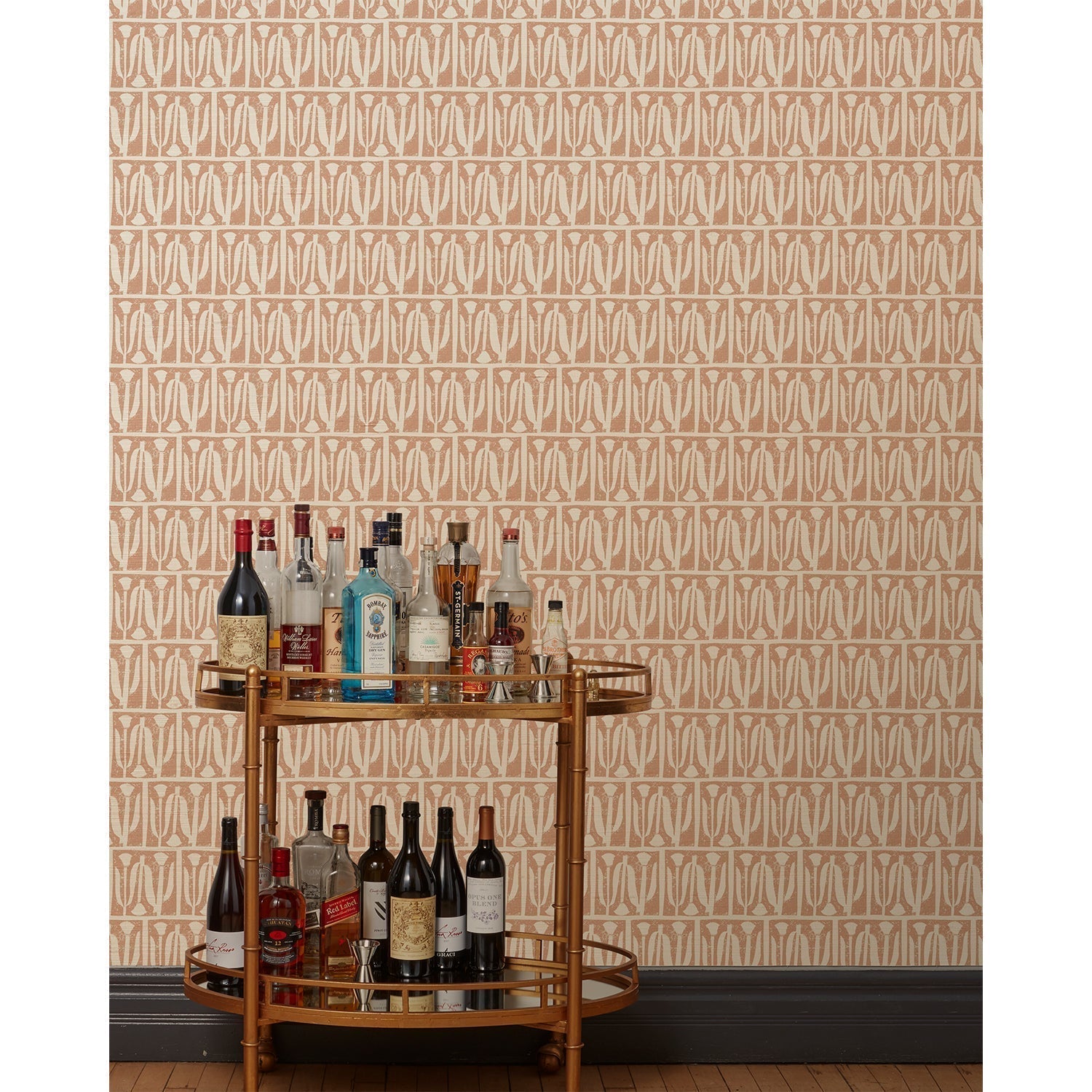 A bronze bar cart in front of a wall papered in an abstract tulip print in a repeating stripe on a rust field.