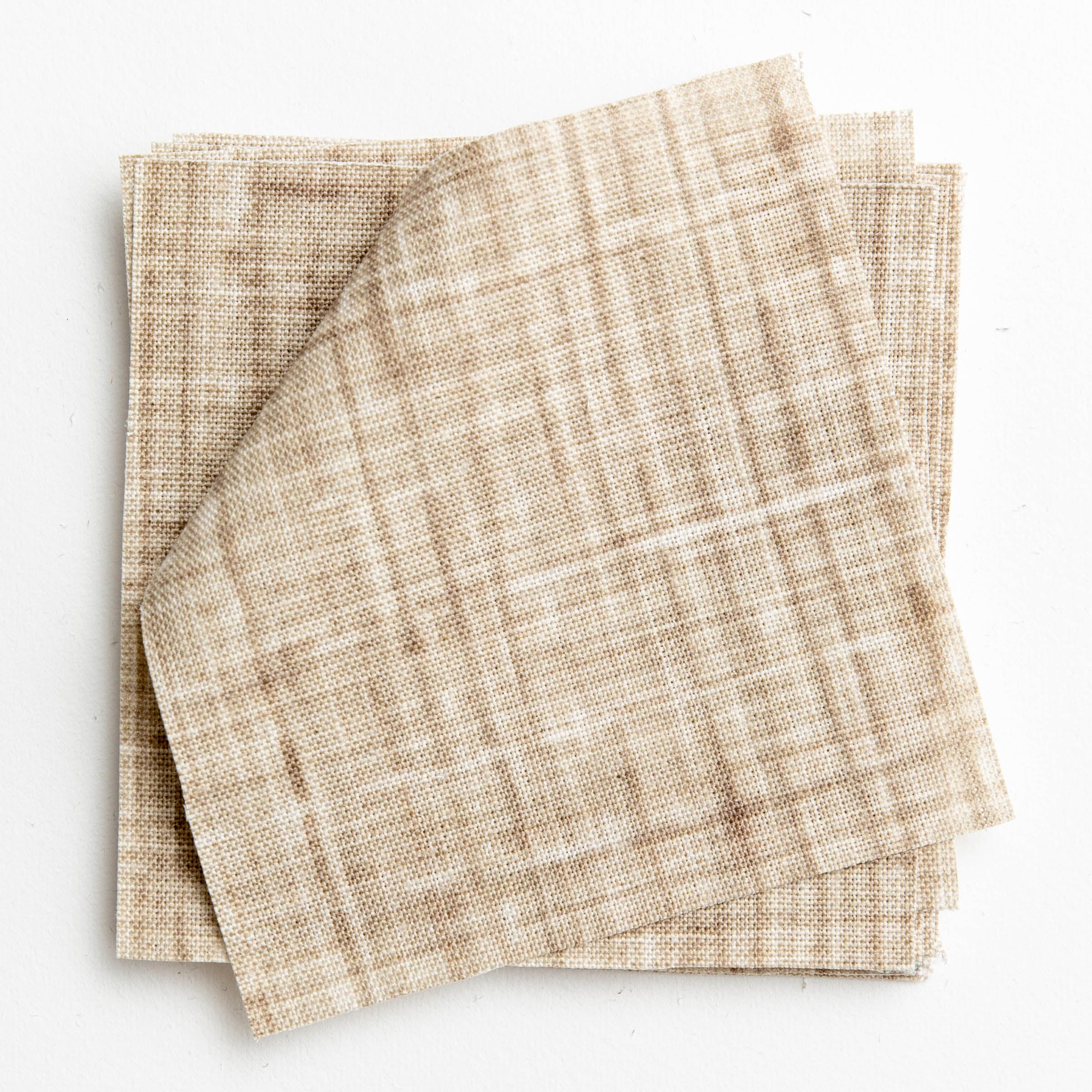 A stack of fabric swatches in a textured tweed pattern in shades of tan.