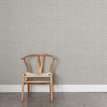 A wooden chair stands in front of a wall papered in a textured tweed pattern in shades of gray. 