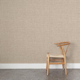 A wooden chair stands in front of a wall papered in a textured tweed pattern in shades of tan.