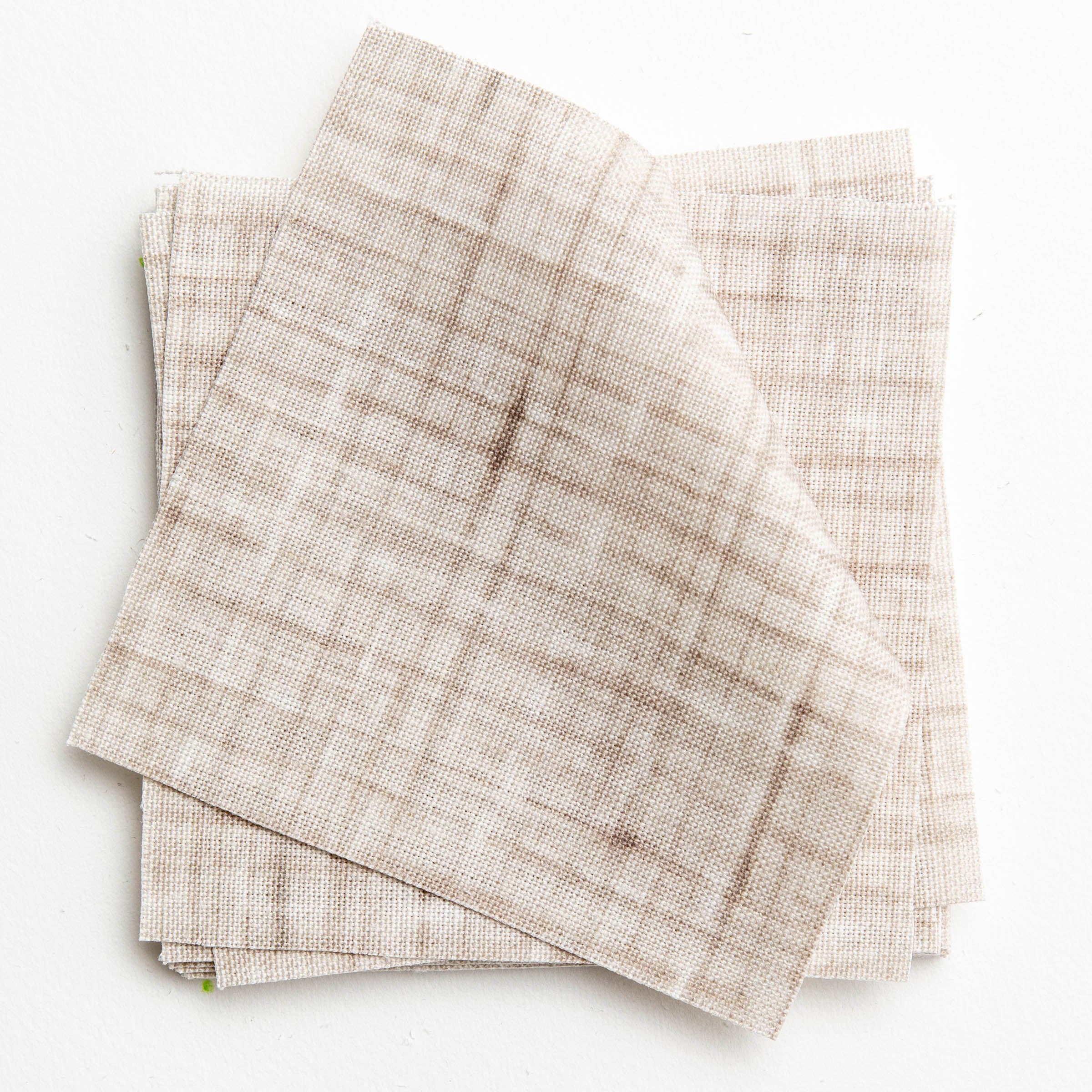 A stack of fabric swatches in a textured tweed pattern in shades of cream and brown.