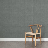 A wooden chair stands in front of a wall papered in a textured tweed pattern in shades of gray-green.