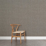 A wooden chair stands in front of a wall papered in a textured tweed pattern in shades of brown and gray.