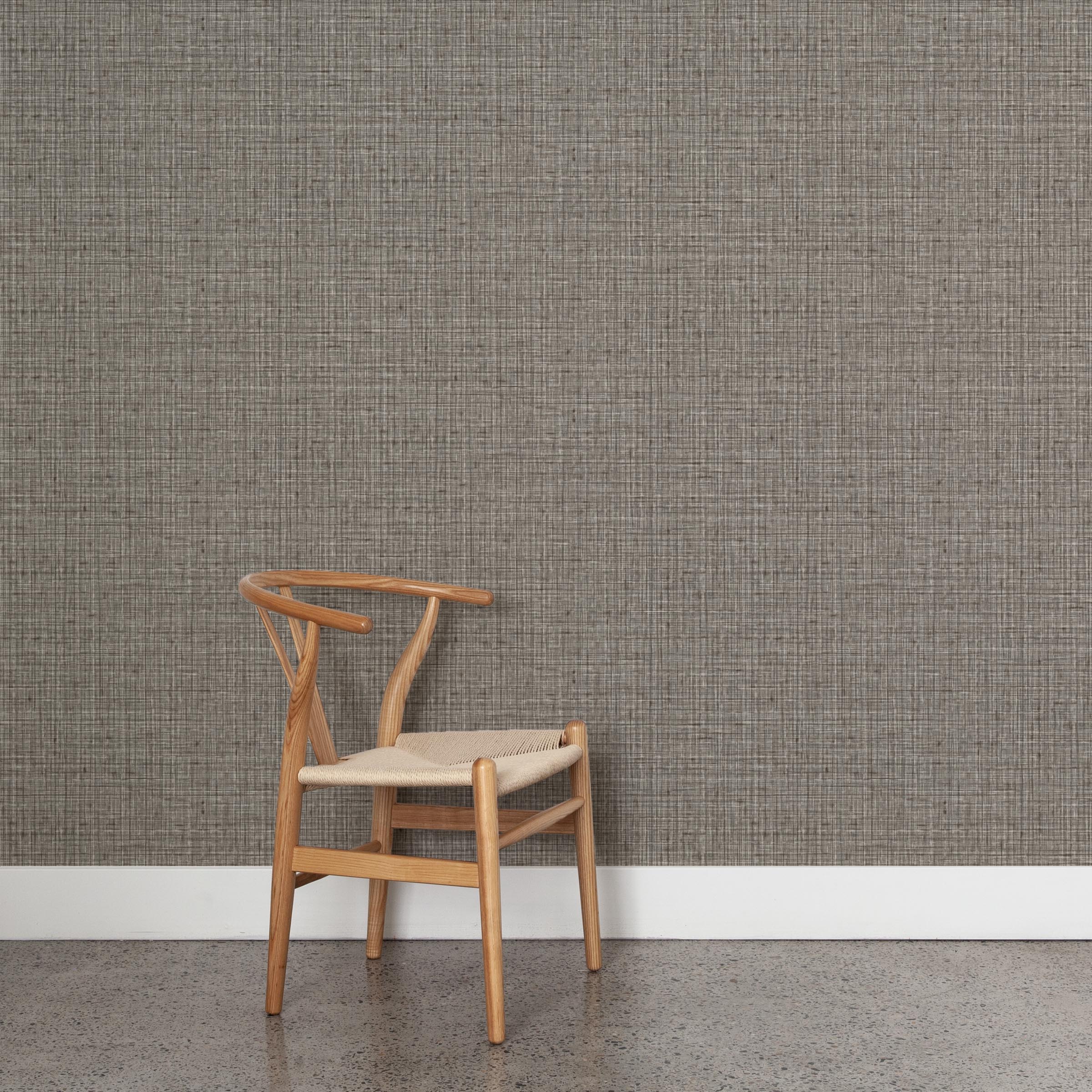 A wooden chair stands in front of a wall papered in a textured tweed pattern in shades of brown and gray.