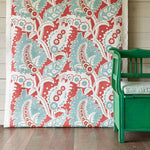 A green bench stands in front of a wall draped in fabric yardage in a paisley print in shades of white, red and turquoise.