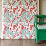 A green bench stands in front of a wall draped in fabric yardage in a paisley print in shades of white, red and turquoise.