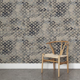A wooden chair stands in front of a wall papered in a diamond checked pattern in shades of cream, blue and gray.