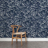 A wooden chair stands in front of a wall papered in a playful wave print in white on a navy watercolor field.