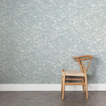 A wooden chair stands in front of a wall papered in a playful wave print in white on a light blue watercolor field.