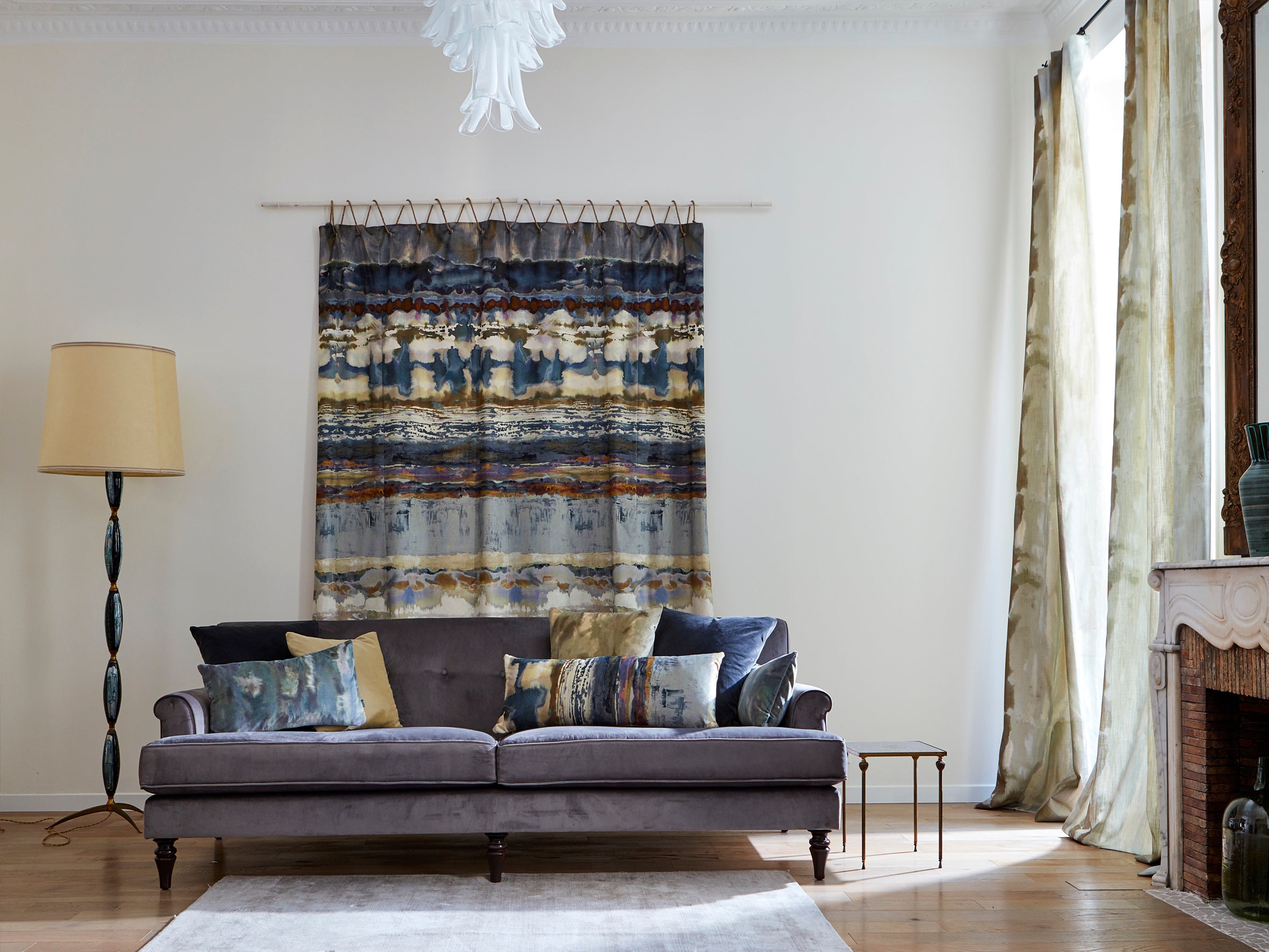 A living room with a hanging textile and throw pillows in the same abstract paint swatch print.