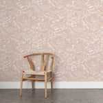 A wooden chair stands in front of a wall papered in a playful wave print in white on a light pink watercolor field.