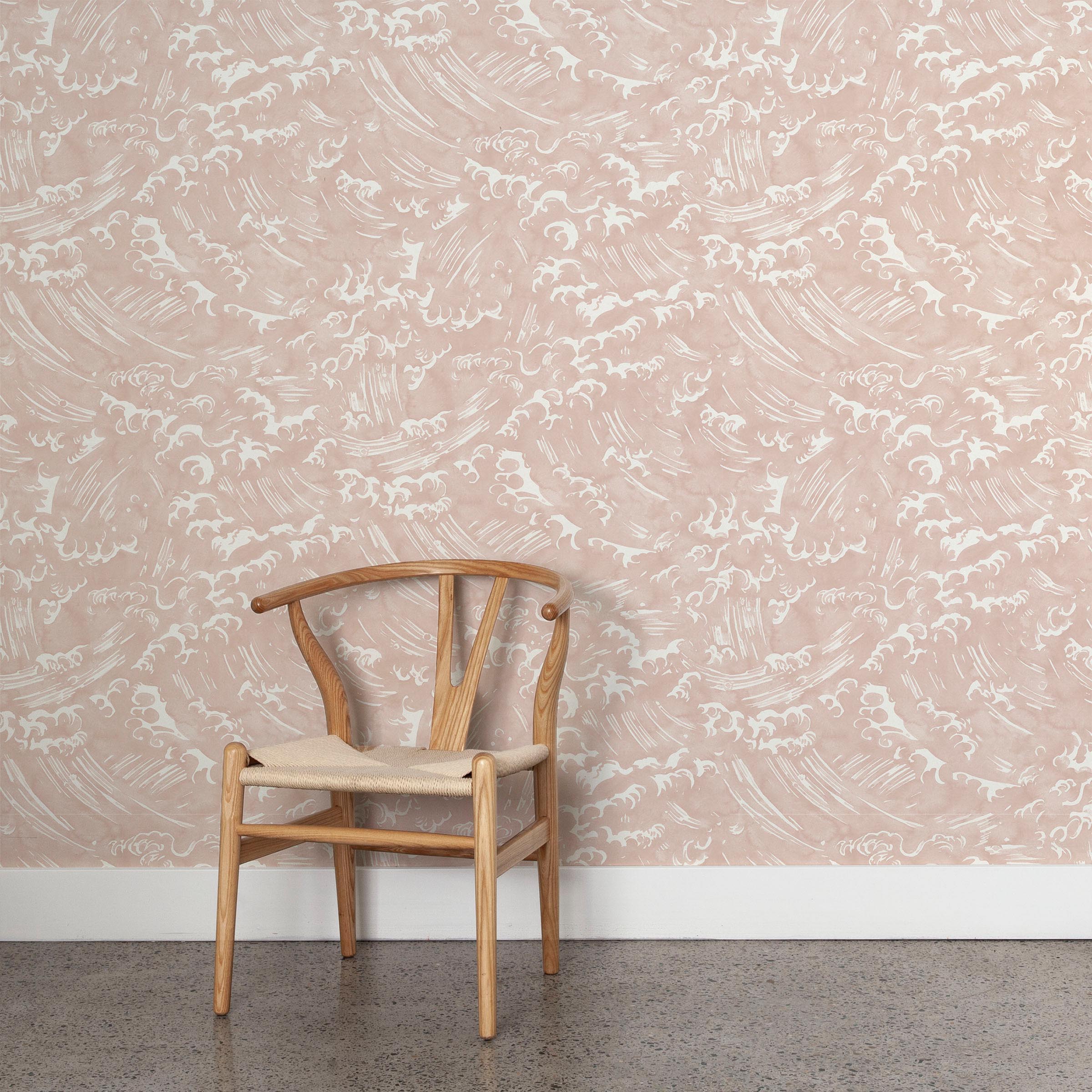 A wooden chair stands in front of a wall papered in a playful wave print in white on a light pink watercolor field.
