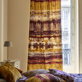 A sunny bedroom with curtains and throw pillows all in the same abstract paint swatch print.