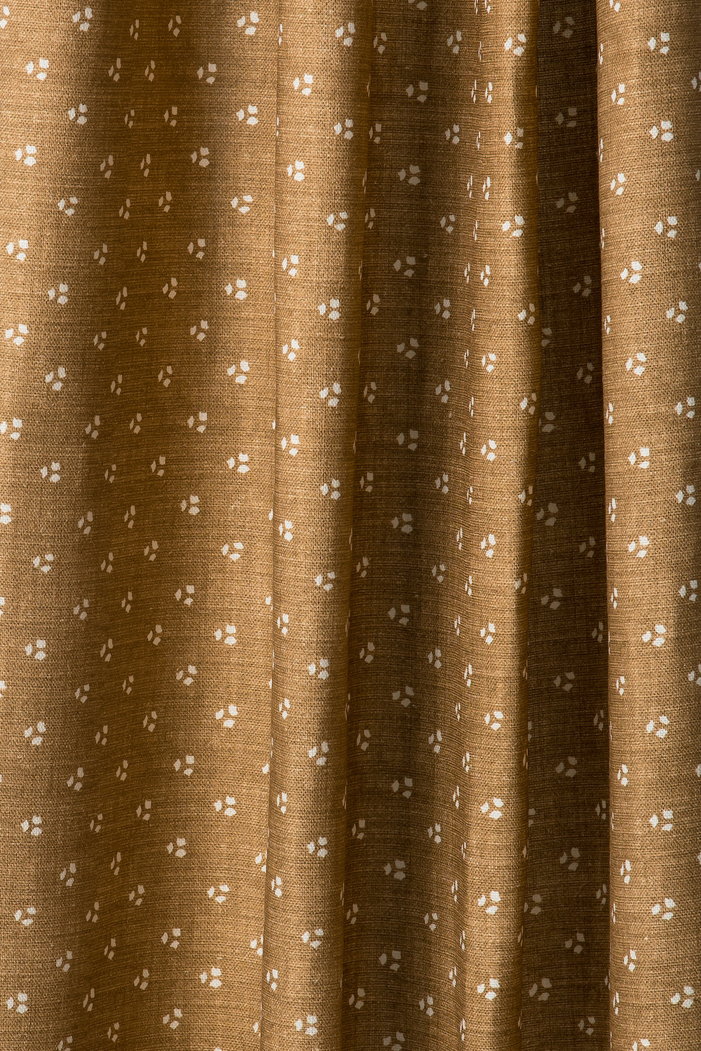 Draped printed fabric in a clustered dot pattern in cream on a camel field.