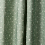 Draped printed fabric in a clustered dot pattern in cream on a sage field.