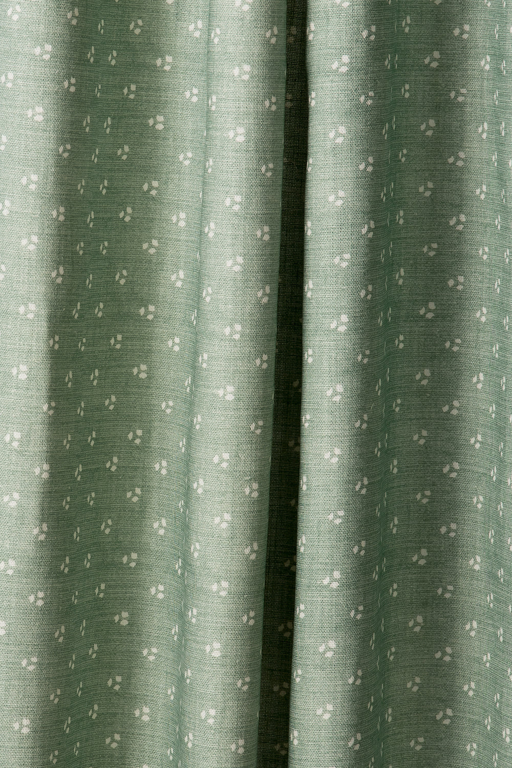 Draped printed fabric in a clustered dot pattern in cream on a sage field.