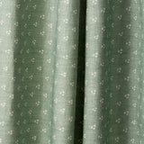 Draped printed fabric in a clustered dot pattern in cream on a sage field.