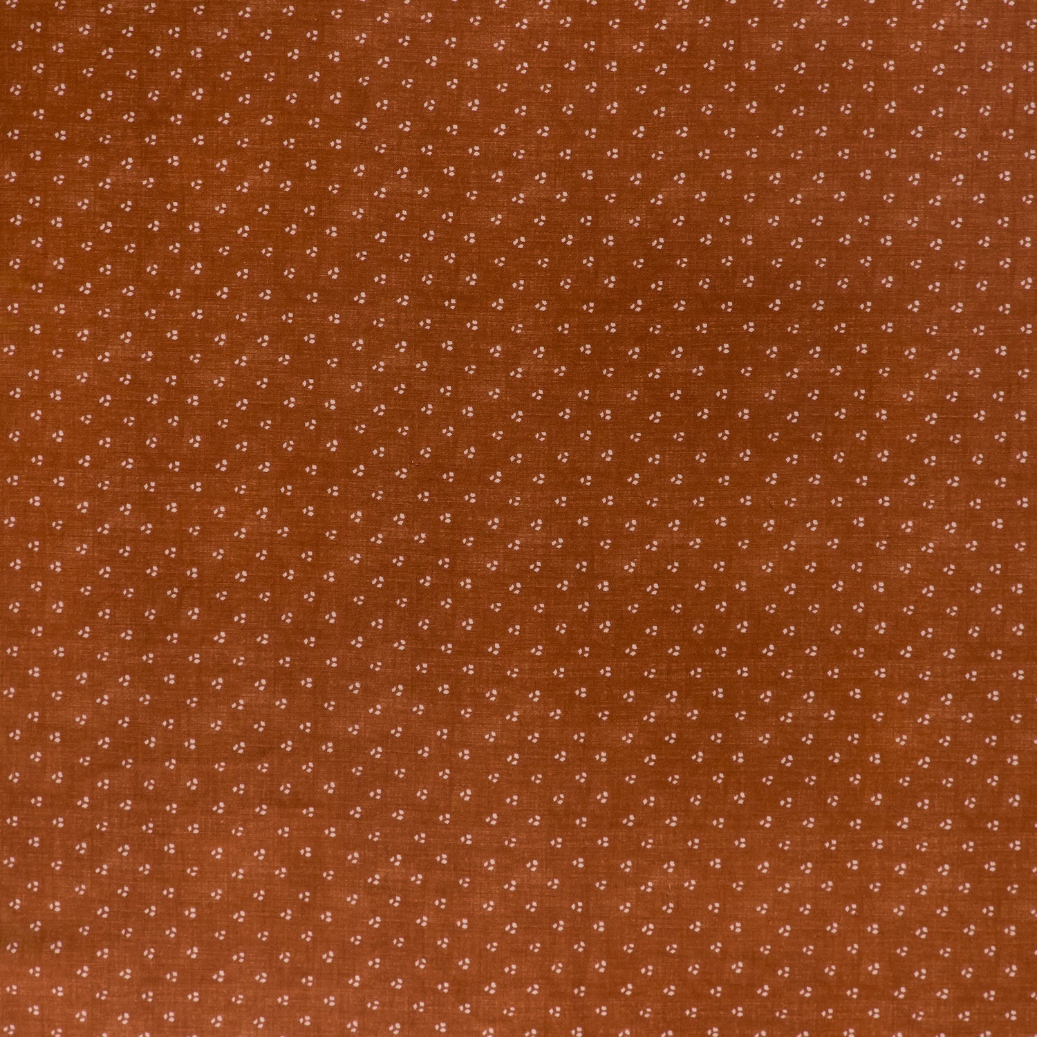 printed linen fabric in a clustered dot pattern in beige on a burnt orange field.