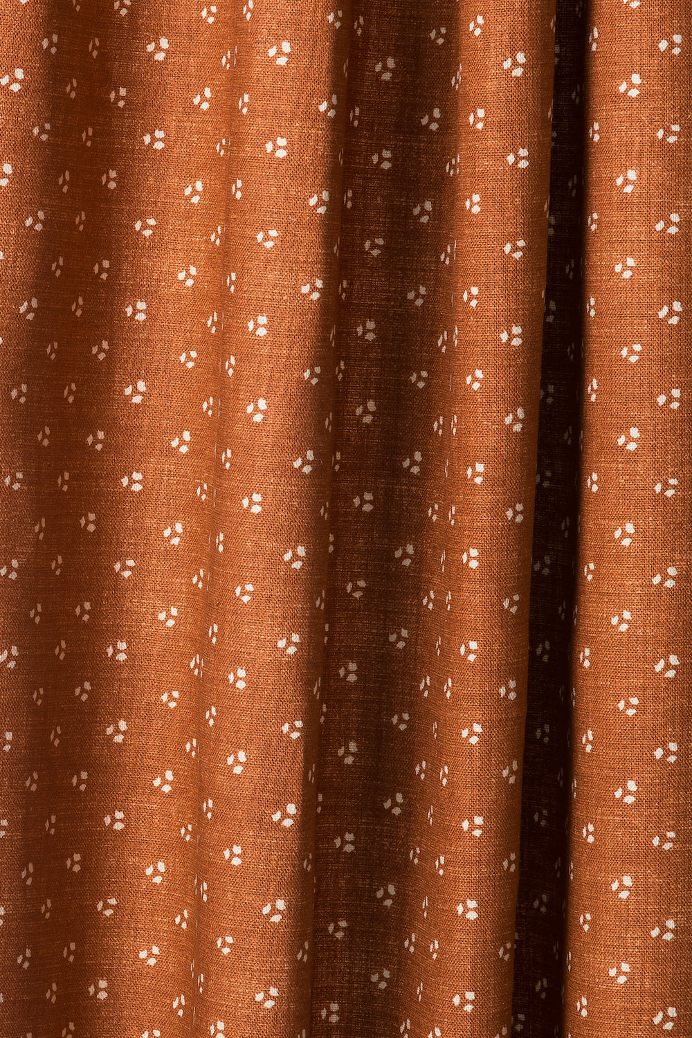 Draped printed fabric in a clustered dot pattern in beige on a burnt orange field.